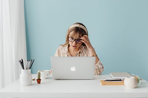 Free Woman wearing glasses working intently on a laptop at a bright, tidy desk. Stock Photo