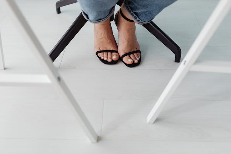 Womans Feet In Black High Heel Sandals On White Floor Under A Table