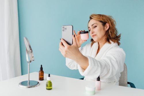 Free Woman in bathrobe taking a skincare selfie with products on desk. Stock Photo