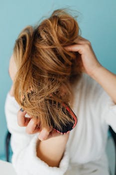 Close-up of a woman brushing her blonde hair in a casual setting.