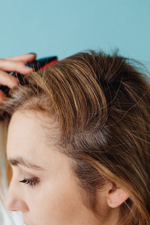 Free Close-up of a woman brushing her hair against a blue background in a studio setting. Stock Photo