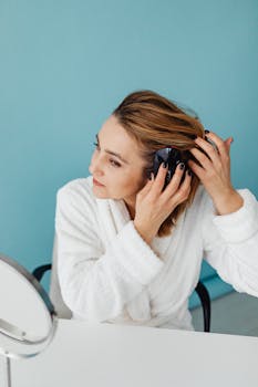 Woman in a white robe brushes her hair with a blue background.