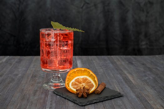 Chilled red cocktail with orange slice and spices on a dark wooden surface, perfect for vibrant gatherings.