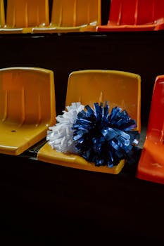 Cheerleading pom poms on colorful stadium seats in an empty arena, conveying excitement.
