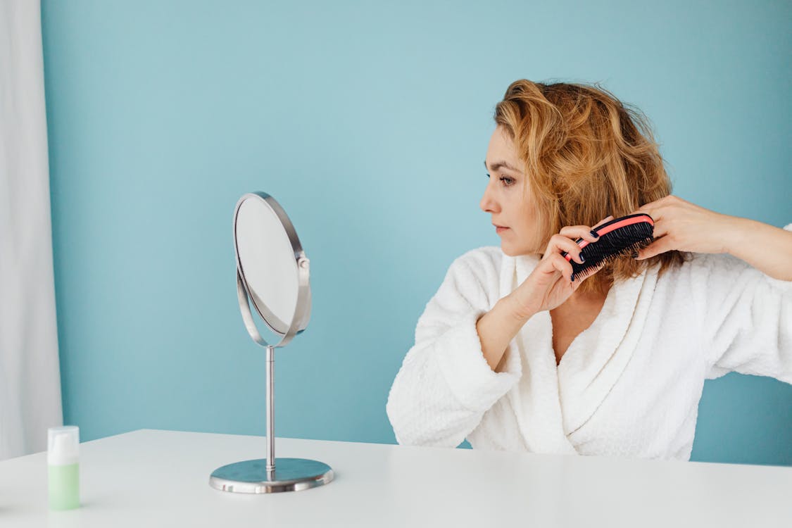 A Woman Combing Her Hair while Looking at a Mirror · Free Stock Photo