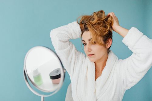 Free Woman in bathrobe looks in mirror while styling hair, in a modern indoor setting. Stock Photo