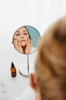 Adult woman applies skincare while looking in a mirror, emphasizing self-care.