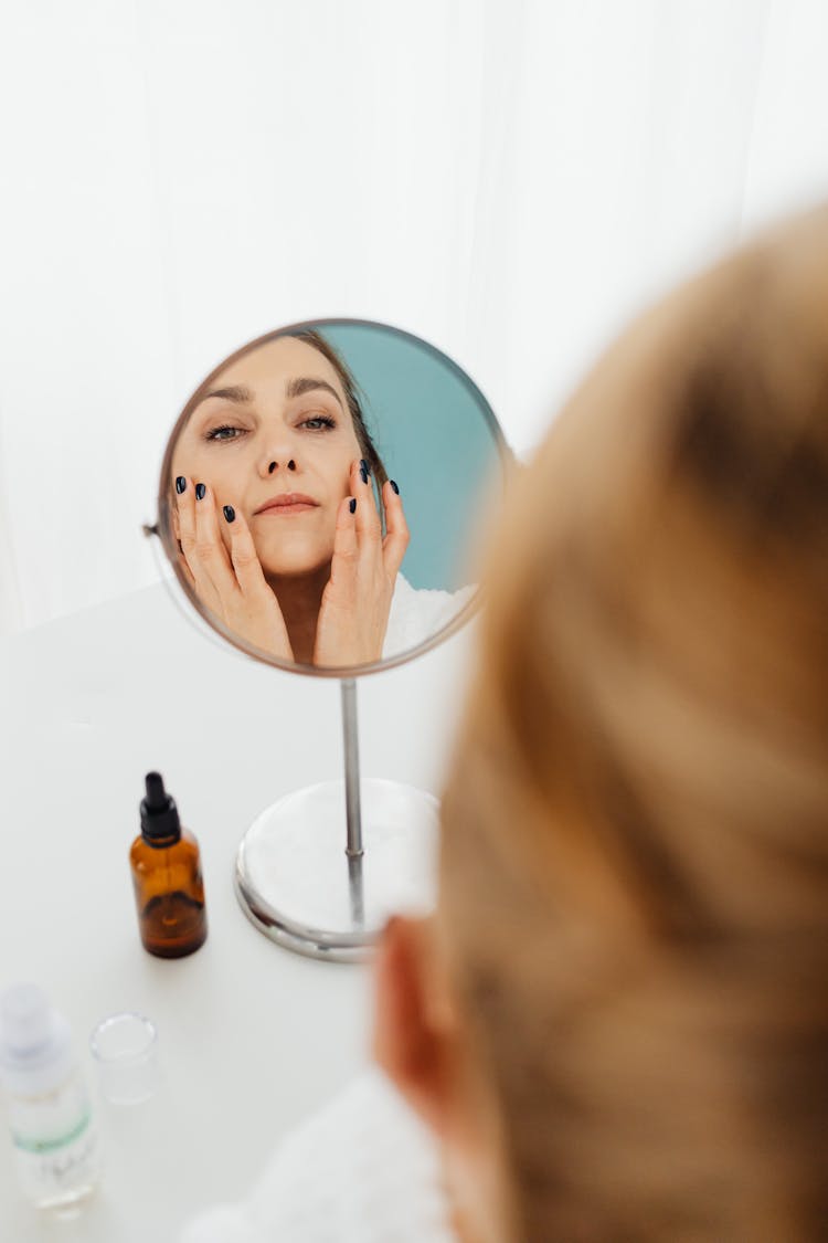 

A Woman Applying Skincare While Looking At A Mirror