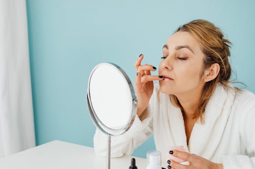 Free A Woman in White Bathrobe Applying a Cream on Her Lips Using Her Fingers Stock Photo
