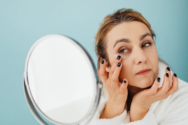 A Woman Looking At The Mirror While Applying A Cream On Her Face