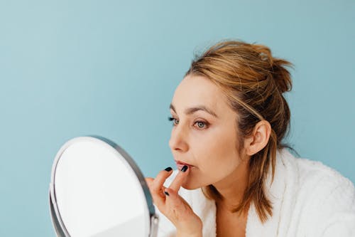 Free A Woman Applying a Cream on Her Lips while Looking at the Mirror Stock Photo