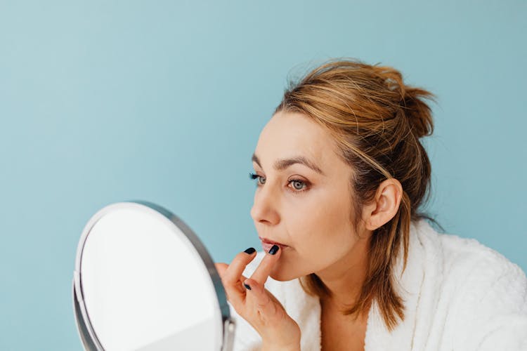 A Woman Applying A Cream On Her Lips While Looking At The Mirror