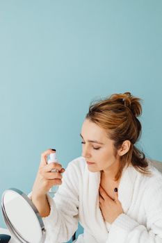 A woman in a bathrobe uses a facial spray for skincare in a serene setting.
