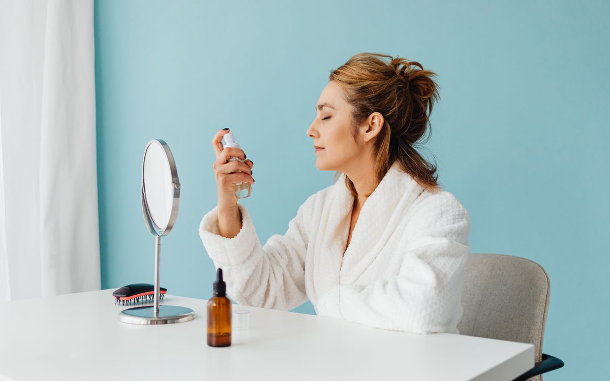 Woman in bathrobe using a spray bottle for skincare during a self-care routine indoors.
