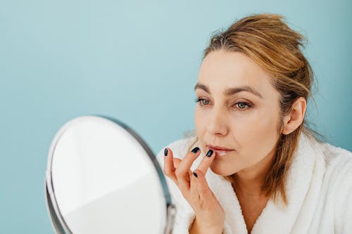 Free A Woman Applying a Cream on Her Lips while Looking at the Mirror Stock Photo