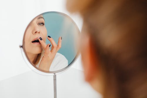 Free A Woman Looking at the Mirror while Applying a Cream on Her Lips Stock Photo
