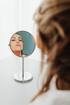 A woman gazes into a circular mirror, capturing a serene reflection indoors.