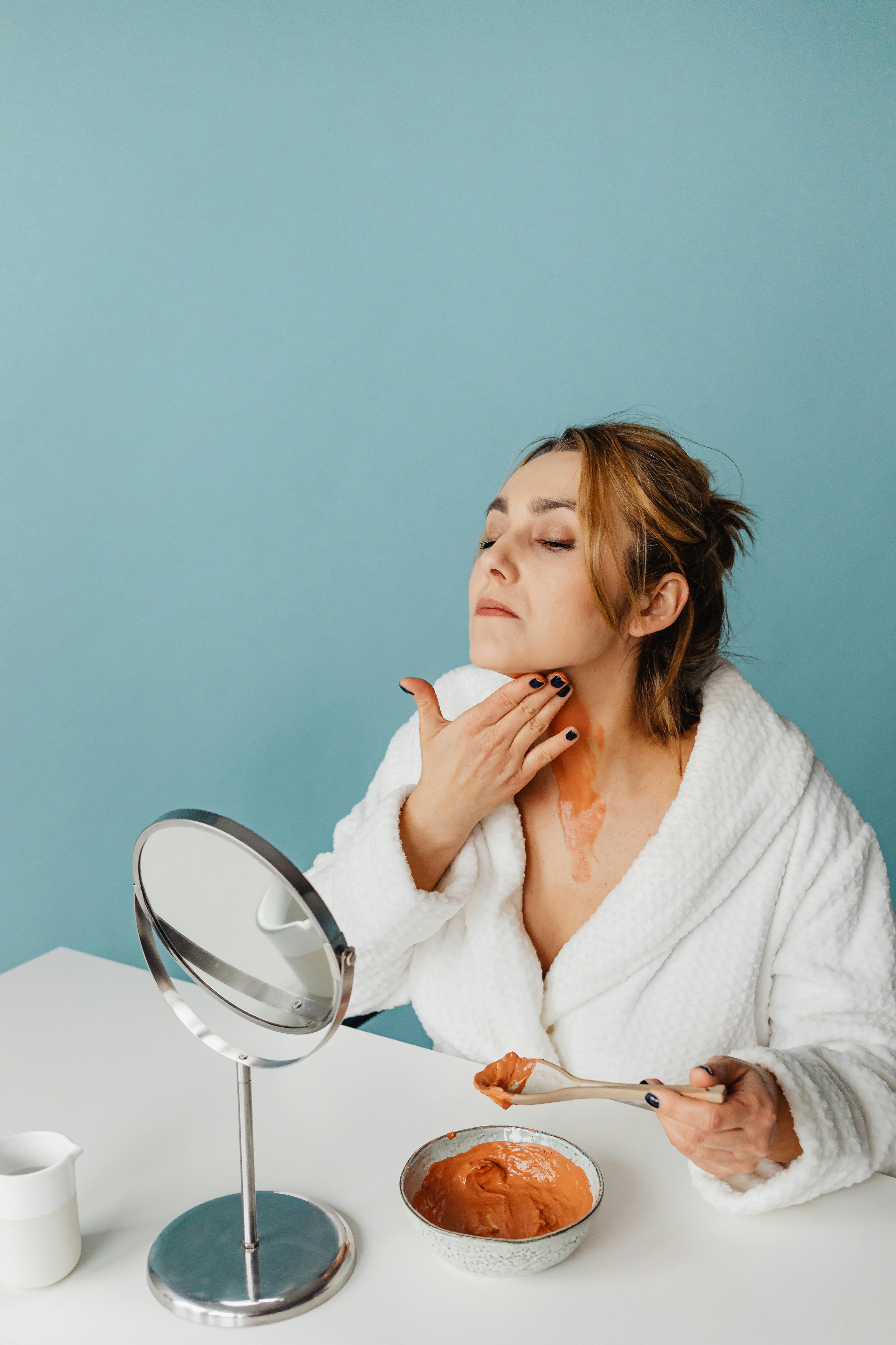 woman in bathrobe spreading cream on neck