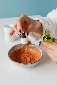 Woman preparing a homemade clay facial mask by adding drops of cosmetic oil.