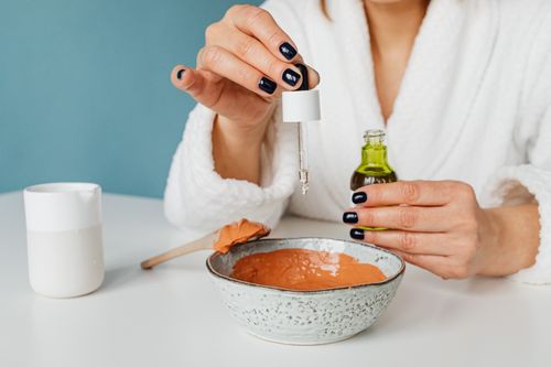 Free A woman in a bathrobe mixing ingredients for a DIY skincare mask using a pipette. Stock Photo
