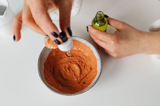 Close-up of hands blending clay mask with skincare essence in minimalist setting.
