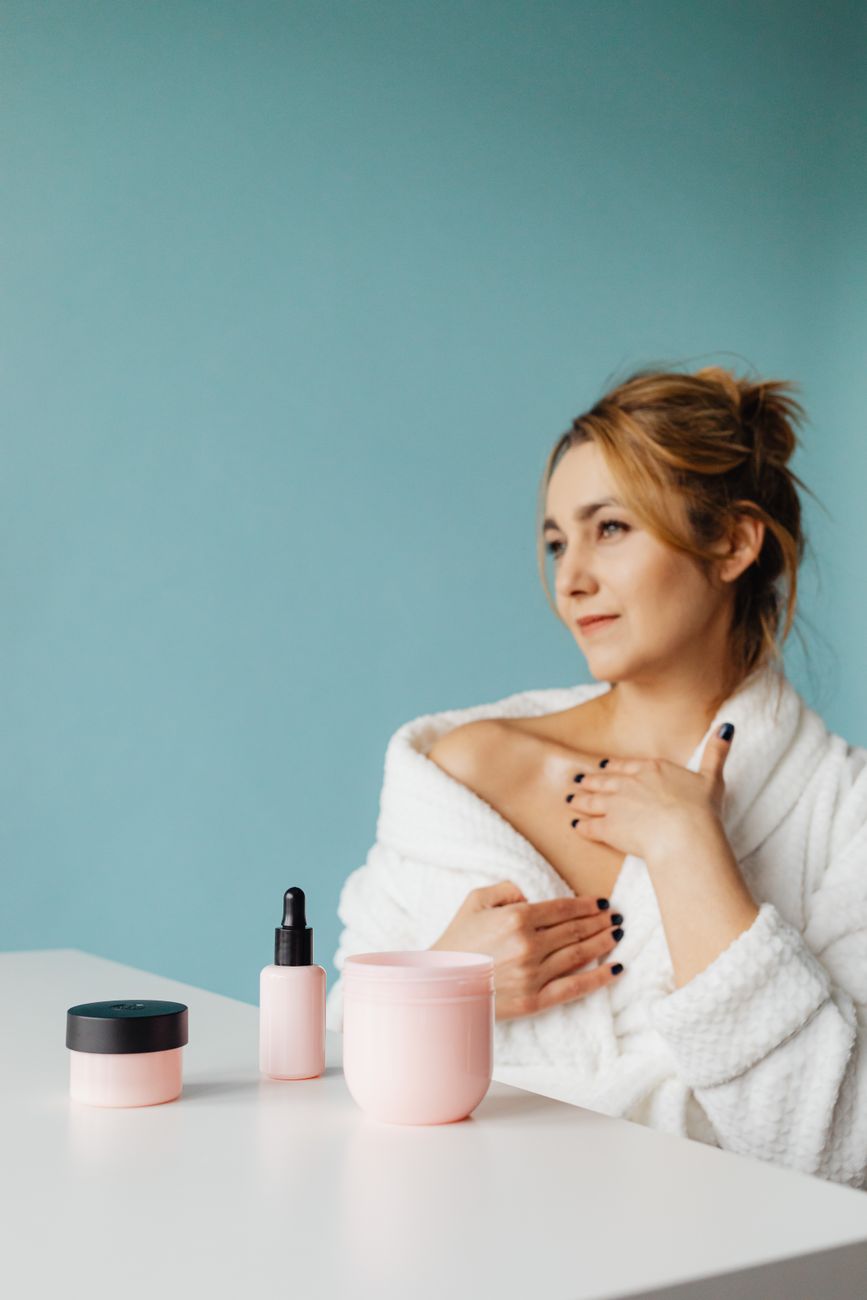Woman enjoying relaxing skincare routine in a bathrobe with pastel products.
