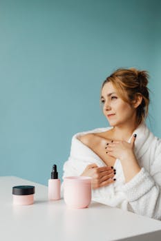 Woman enjoying relaxing skincare routine in a bathrobe with pastel products.