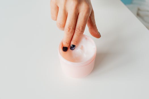 Close-up of a hand with painted nails dipping into a jar of face cream, representing self-care.