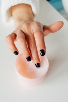 A close-up shot of a woman's hand with black-painted nails applying a moisturizing cream.