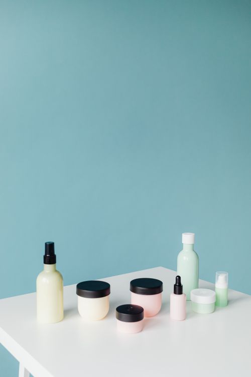 Free Aesthetic arrangement of skincare bottles and jars on a table with a blue background. Stock Photo