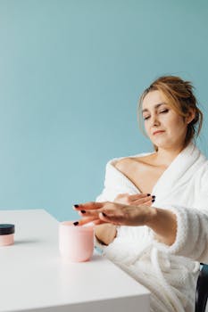 Woman enjoying leisure time in bathrobe applying hand cream against a blue background.