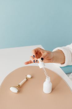 Close-up of a woman's hand holding a dropper bottle and jade roller on a stylish background.