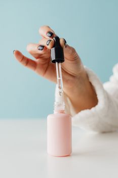 A detailed shot of a dropper dispensing liquid from a skincare bottle against a blue background.