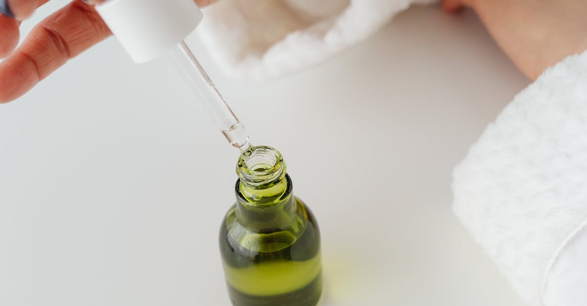 Close-up of hands with manicured nails holding a dropper over a green serum bottle. Close-up of hands with manicured nails holding a dropper over a green serum bottle.