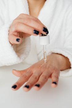 A close-up of a hand applying skincare serum with a dropper indoors.