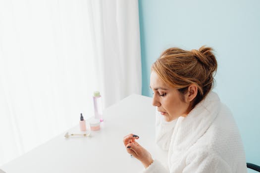 Woman wearing a bathrobe applying skincare products indoors, focusing on her daily beauty routine.