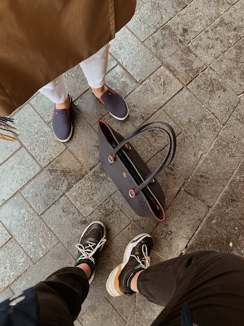 Free Top View of Fashionable Man and Woman Standing on a Sidewalk and a Bag Standing Between Them  Stock Photo