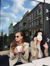 Two Woman in Long Trench Coat Jackets Drinking Coffee Together