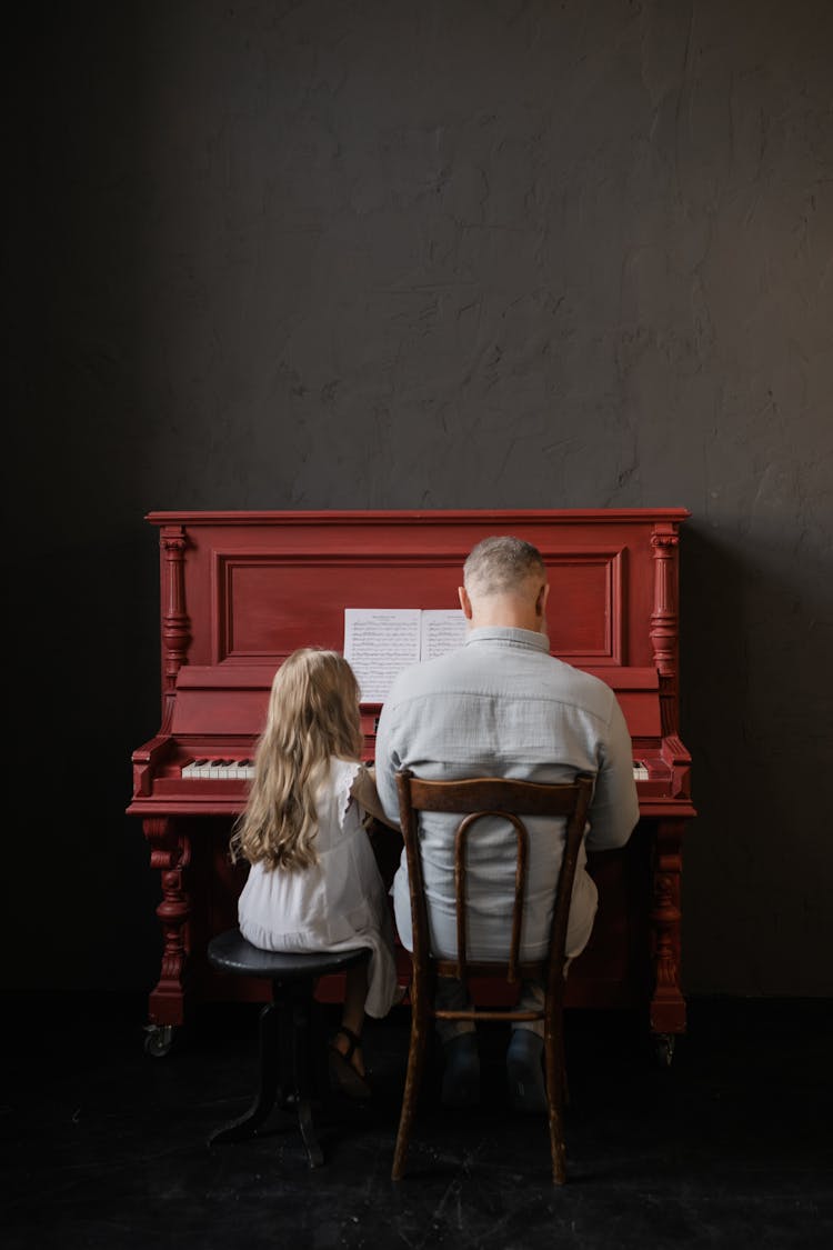 Back View Of Grandfather And Granddaughter Playing The Piano