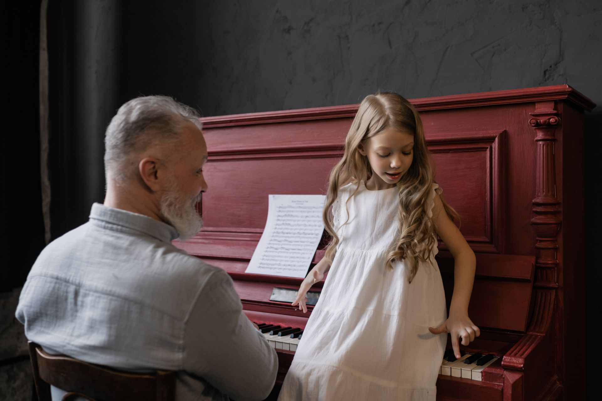 A grandfather and granddaughter share a musical moment at a piano, embodying family bonding and learning.