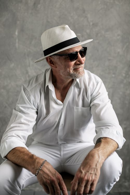 Free Elderly man wearing a fedora and sunglasses, posing confidently in a studio setting. Stock Photo
