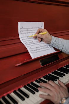 Close-up of a composer revising sheet music on a red piano.