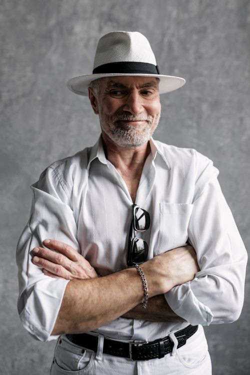 Free Elderly man with a white fedora smiling confidently in a studio portrait, arms crossed and wearing a white shirt. Stock Photo