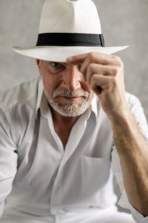 Free Close-up portrait of an elderly man wearing a white fedora and dress shirt in a studio setting. Stock Photo