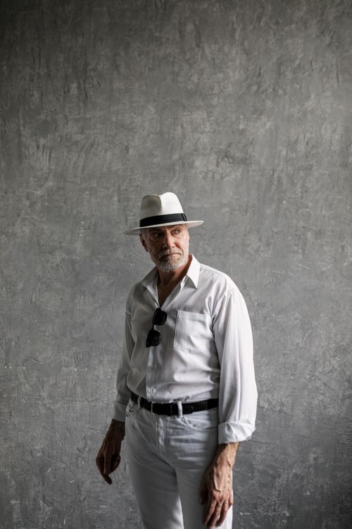Free Elegant senior gentleman modeling in white attire with a fedora hat against a gray studio background. Stock Photo