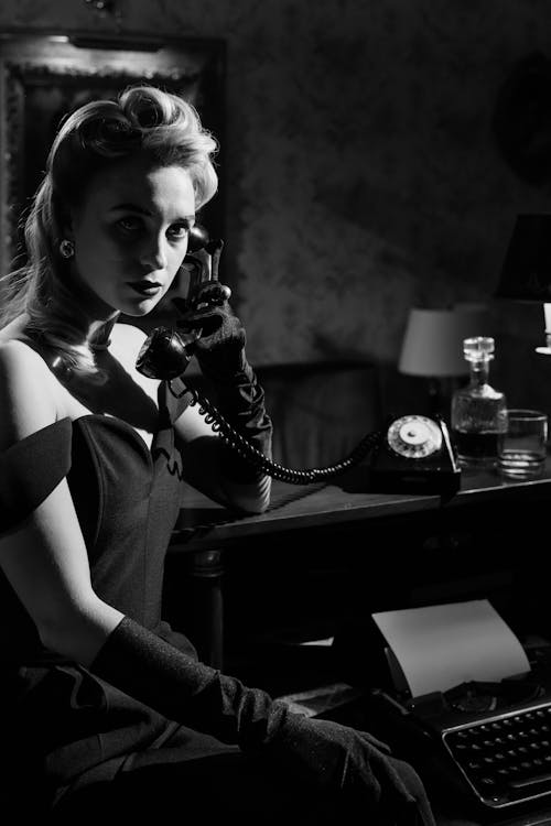 Photo of Woman Sitting Beside Counter Using A Rotary Phone