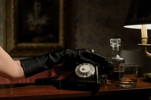 A vintage setup featuring a rotary phone, whiskey glass, and black-gloved hands in low light.