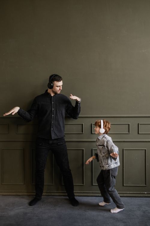 Free A joyful moment of a father and son dancing indoors with wireless headphones, showcasing family bonding. Stock Photo