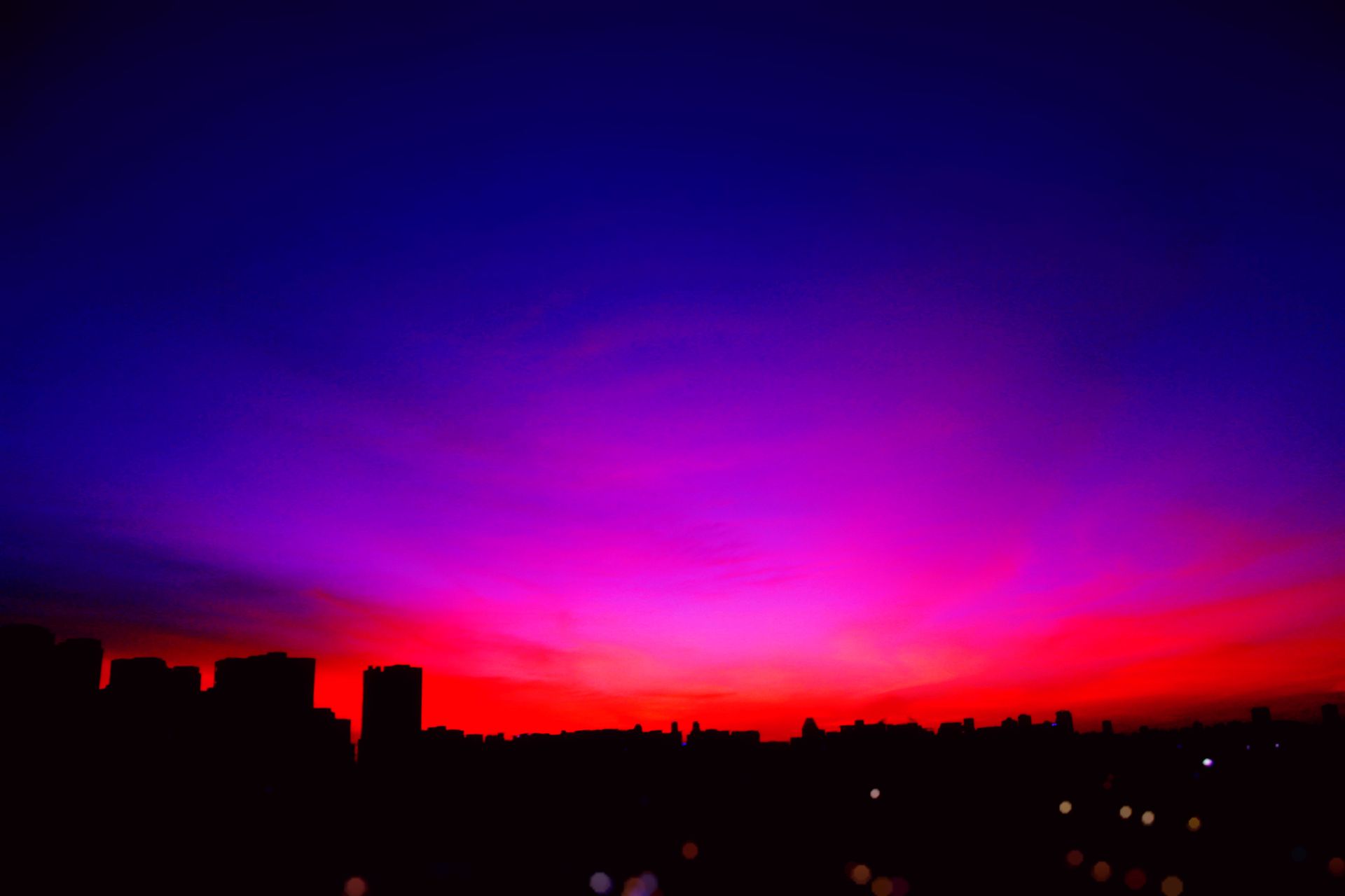 A colorful sunset paints the sky over an urban skyline, creating a dramatic silhouette.