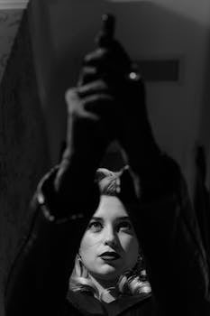 Black and white photo of a mysterious femme fatale holding a gun, evoking film noir style.